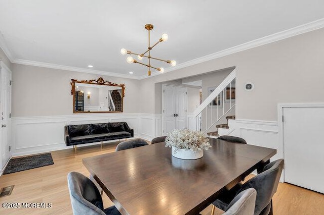 dining room featuring a wainscoted wall, light wood-type flooring, ornamental molding, and a chandelier