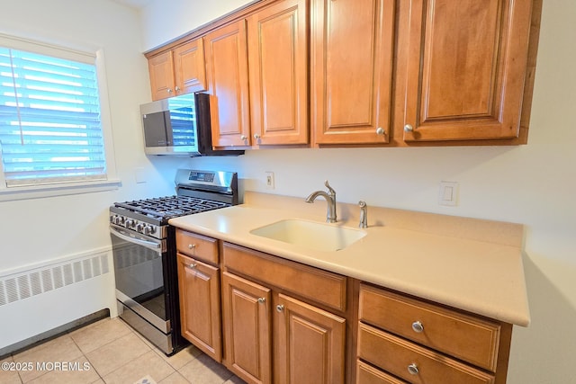 kitchen with a sink, radiator, appliances with stainless steel finishes, light tile patterned flooring, and light countertops
