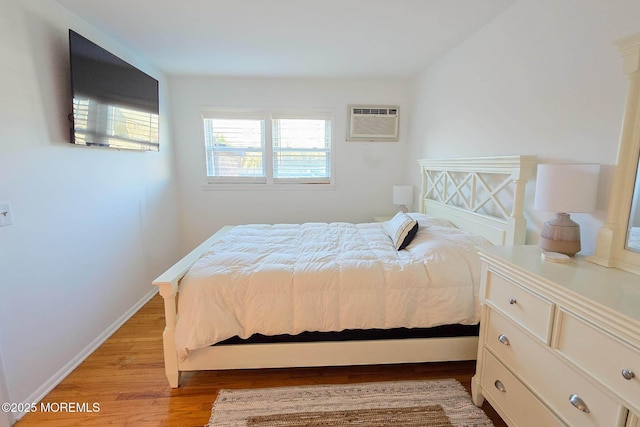 bedroom featuring baseboards, light wood-style floors, and a wall unit AC