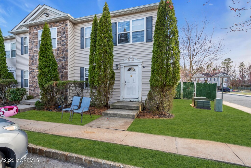view of front facade featuring stone siding, central AC unit, and a front lawn