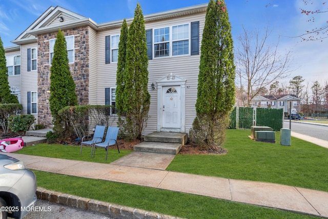 view of front facade featuring stone siding, central AC unit, and a front lawn