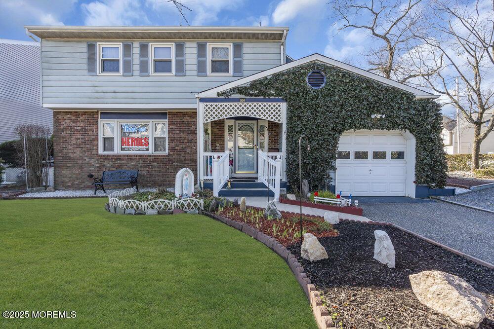 304 E 7th St, Lakewood, NJ 08701 - view of front facade with driveway, an attached garage, brick siding, and a front yard