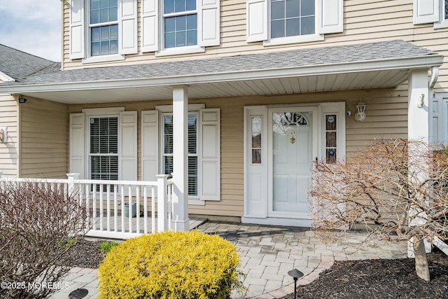 doorway to property featuring a porch and roof with shingles