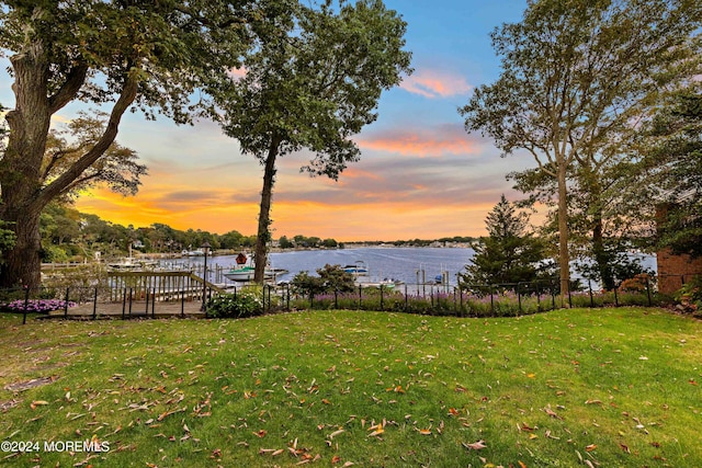 view of yard with a water view, fence, and a boat dock