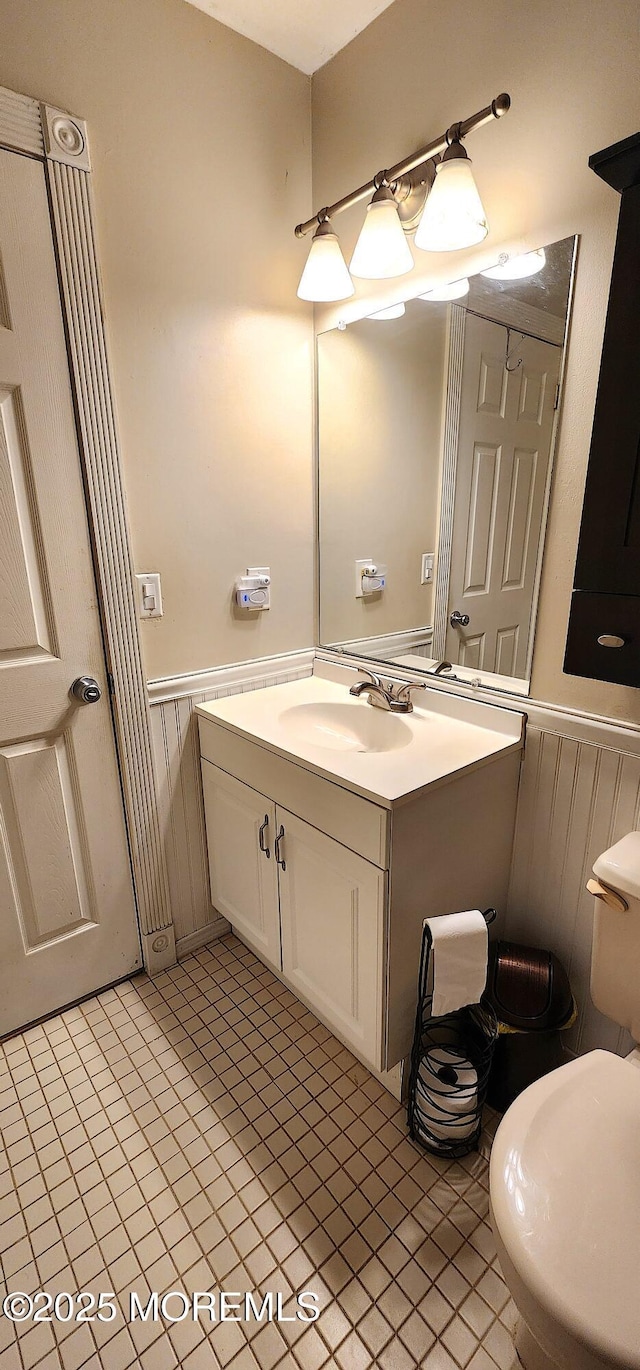 half bathroom featuring a wainscoted wall, tile patterned floors, vanity, and toilet