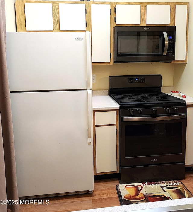 kitchen featuring range with gas stovetop, freestanding refrigerator, black microwave, light countertops, and light wood-style flooring