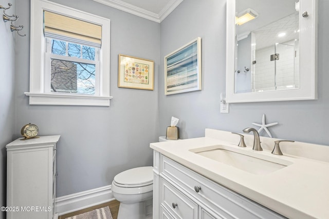 bathroom with a shower stall, vanity, baseboards, toilet, and ornamental molding