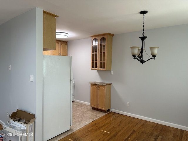 kitchen featuring freestanding refrigerator, glass insert cabinets, light wood-type flooring, and baseboards