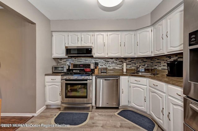 kitchen featuring white cabinetry, appliances with stainless steel finishes, a sink, dark countertops, and decorative backsplash
