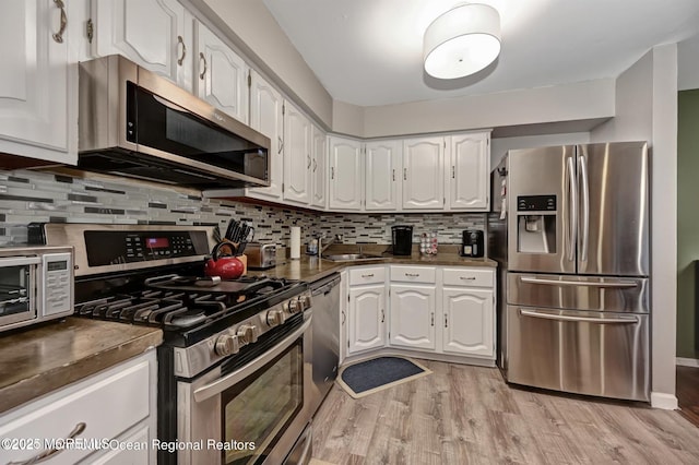 kitchen featuring light wood-style flooring, appliances with stainless steel finishes, dark countertops, and white cabinetry
