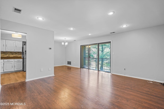 unfurnished living room with an inviting chandelier, dark wood-style floors, visible vents, and recessed lighting