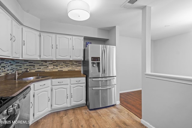 kitchen with stainless steel appliances, tasteful backsplash, white cabinets, and dark countertops