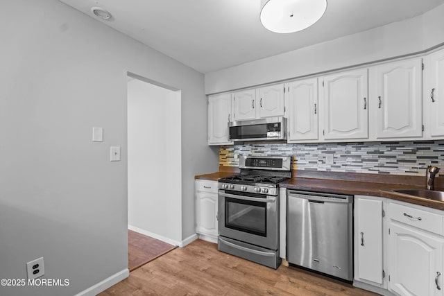 kitchen featuring tasteful backsplash, dark countertops, appliances with stainless steel finishes, light wood-style floors, and white cabinetry
