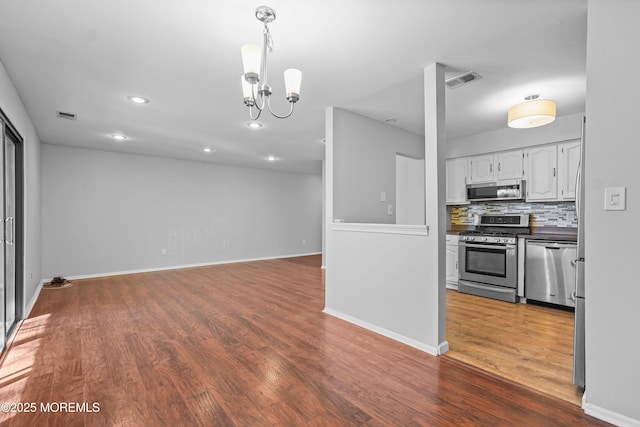 kitchen featuring white cabinetry, backsplash, dark countertops, appliances with stainless steel finishes, and wood finished floors