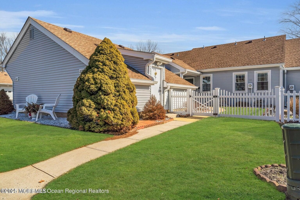 exterior space with a gate, a shingled roof, fence, and a lawn