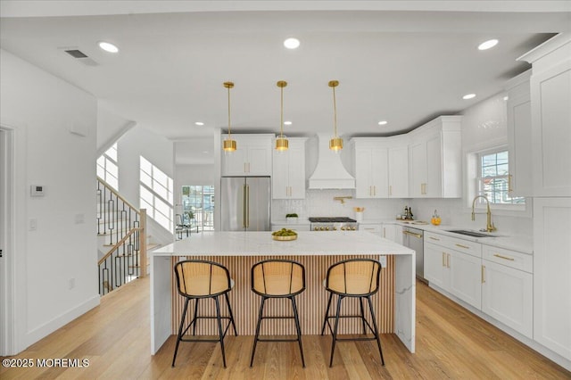 kitchen featuring custom range hood, stainless steel appliances, a sink, visible vents, and light wood-style flooring