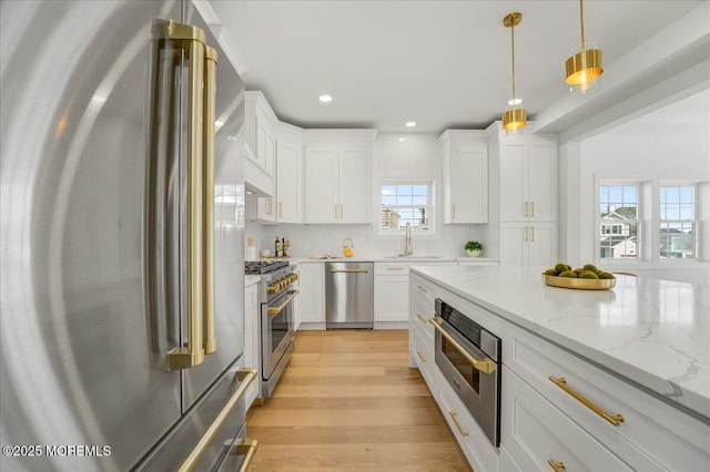 kitchen with high quality appliances, a sink, pendant lighting, white cabinetry, and light wood-type flooring