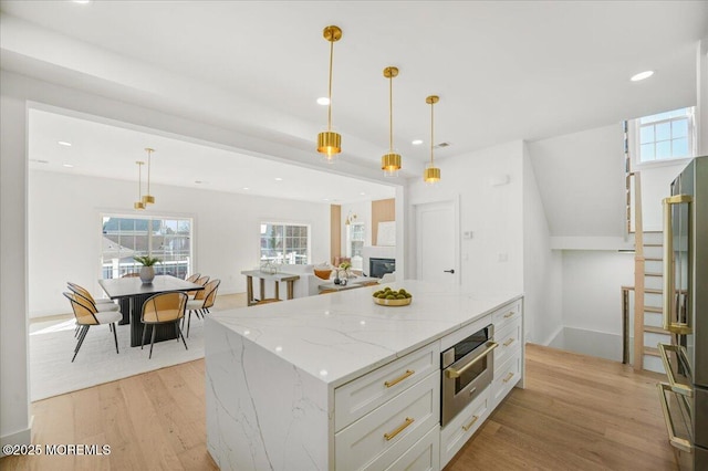 kitchen featuring oven, a kitchen island, white cabinetry, decorative light fixtures, and light wood-style floors
