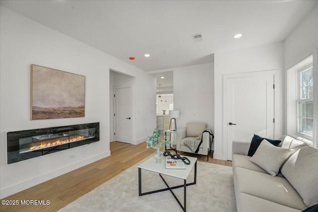 living room with baseboards, visible vents, a glass covered fireplace, and wood finished floors
