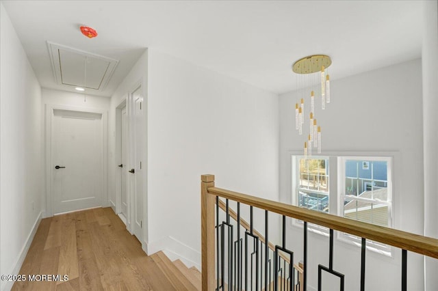 corridor featuring attic access, baseboards, light wood finished floors, and an upstairs landing