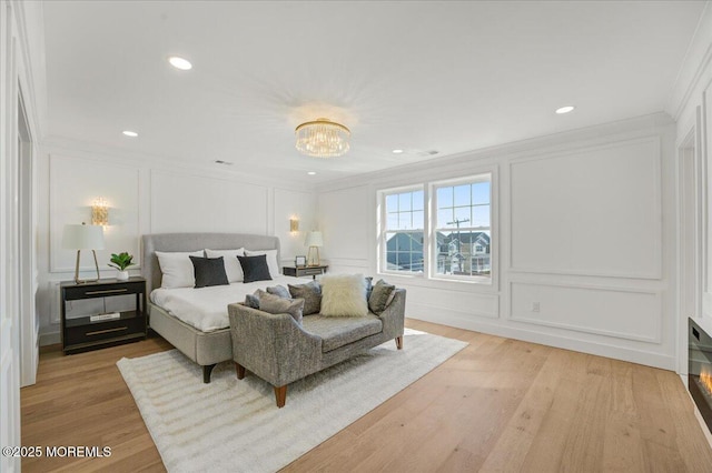 bedroom featuring a notable chandelier, a decorative wall, light wood-type flooring, and crown molding