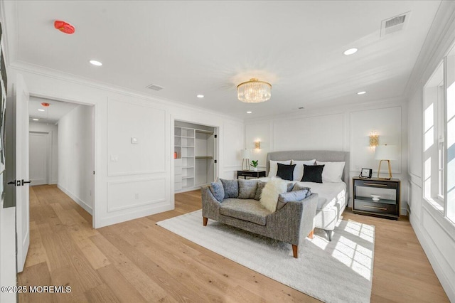 bedroom with a decorative wall, crown molding, and light wood-type flooring