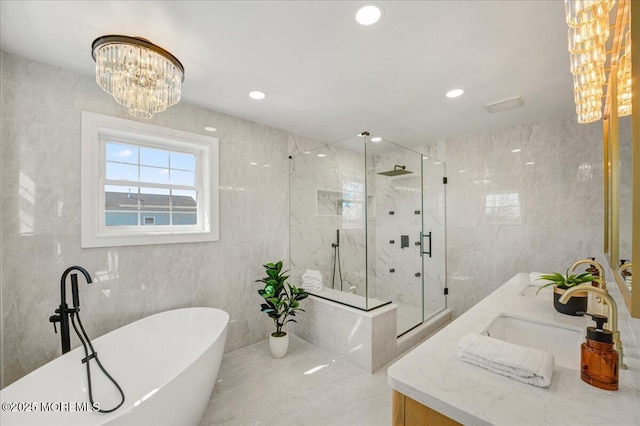 full bathroom featuring a freestanding tub, a sink, a marble finish shower, tile walls, and an inviting chandelier