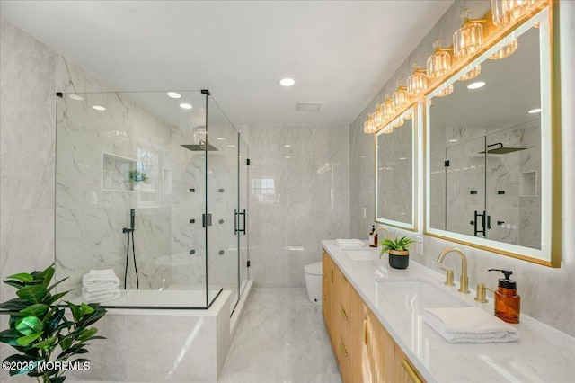 bathroom featuring tile walls, toilet, double vanity, and a marble finish shower