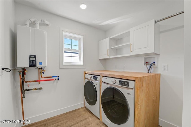 laundry area with tankless water heater, light wood finished floors, baseboards, cabinet space, and washer and clothes dryer