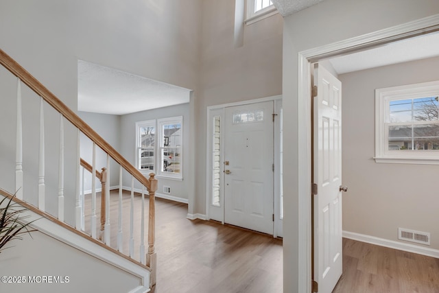 entrance foyer with wood finished floors, a healthy amount of sunlight, stairs, and visible vents