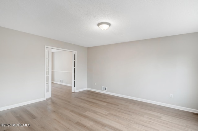 unfurnished room featuring baseboards, visible vents, a textured ceiling, and light wood-style flooring