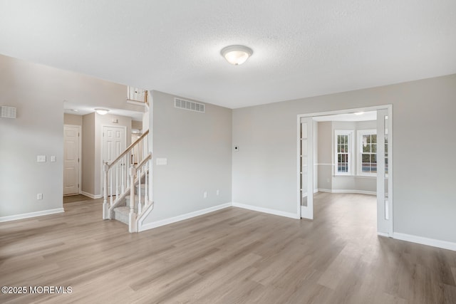 spare room featuring stairs, visible vents, baseboards, and light wood-type flooring