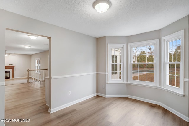 spare room with light wood finished floors, baseboards, and a textured ceiling