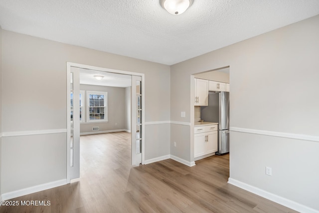 empty room featuring visible vents, baseboards, light wood-style floors, and a textured ceiling