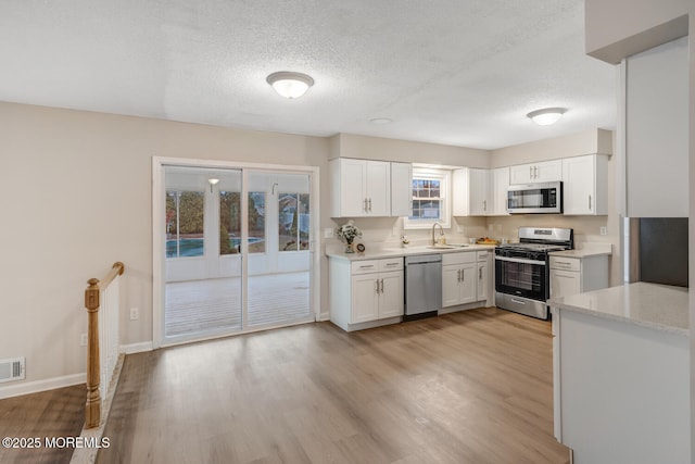 kitchen featuring visible vents, light wood-style flooring, stainless steel appliances, white cabinetry, and a sink