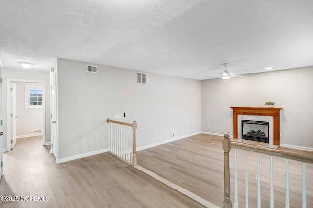 unfurnished living room with a fireplace, visible vents, a ceiling fan, and light wood finished floors