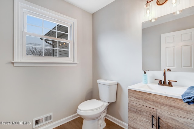 bathroom featuring visible vents, baseboards, toilet, wood finished floors, and vanity