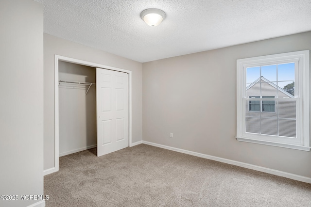 unfurnished bedroom with carpet flooring, a closet, baseboards, and a textured ceiling