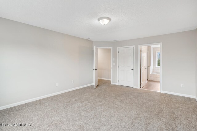 unfurnished bedroom with baseboards, carpet floors, a textured ceiling, and ensuite bath