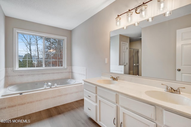 bathroom featuring a bath, double vanity, a sink, and wood finished floors