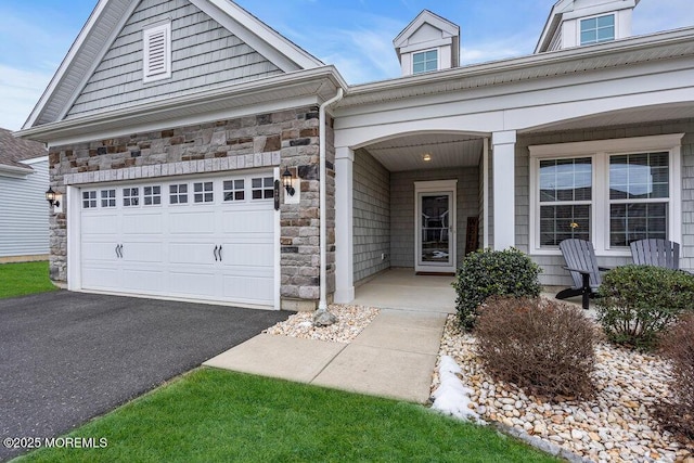 view of front of home featuring covered porch, stone siding, driveway, and a garage