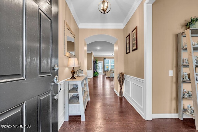 foyer featuring wood finished floors, wainscoting, a decorative wall, arched walkways, and ornamental molding