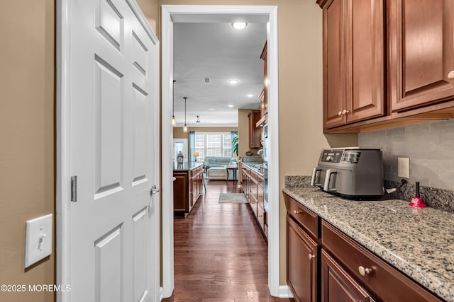 kitchen featuring decorative backsplash, open floor plan, light stone counters, and dark wood finished floors