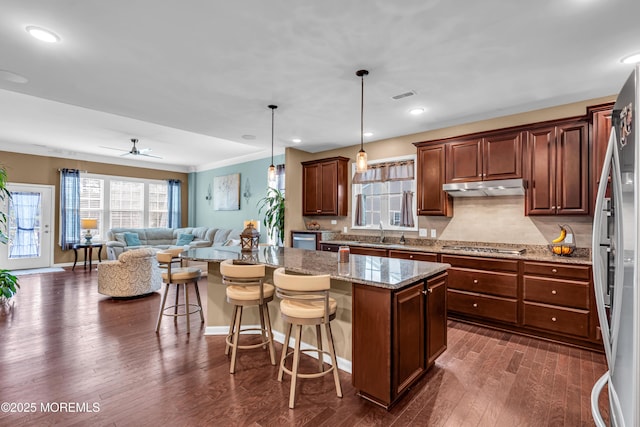 kitchen with dark wood finished floors, tasteful backsplash, under cabinet range hood, a sink, and open floor plan
