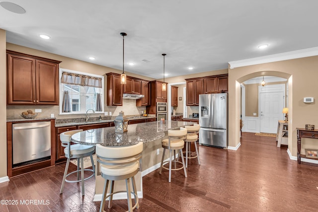 kitchen with a breakfast bar, a center island, stainless steel appliances, arched walkways, and dark wood-type flooring