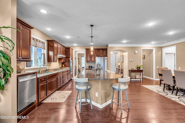 kitchen featuring a kitchen bar, a kitchen island, a sink, arched walkways, and appliances with stainless steel finishes