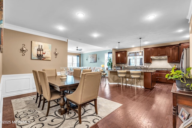 dining space with recessed lighting, dark wood-style flooring, ornamental molding, a wainscoted wall, and a decorative wall