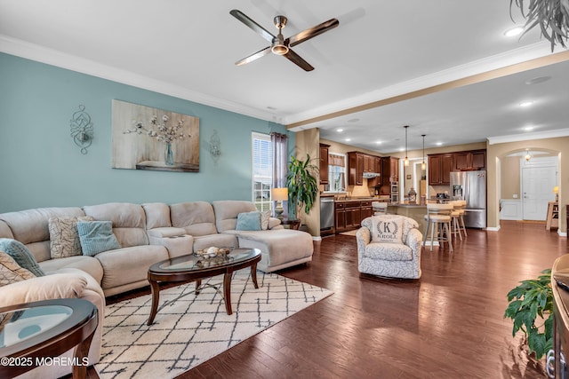living area featuring arched walkways, ceiling fan, ornamental molding, and dark wood-style flooring