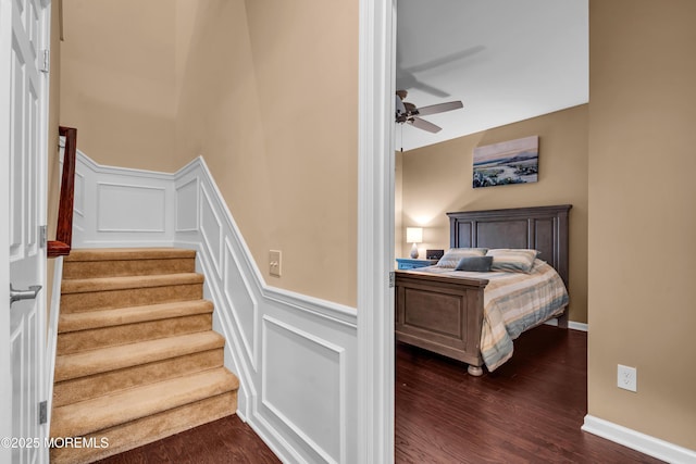 stairway with a decorative wall, wood finished floors, wainscoting, and ceiling fan