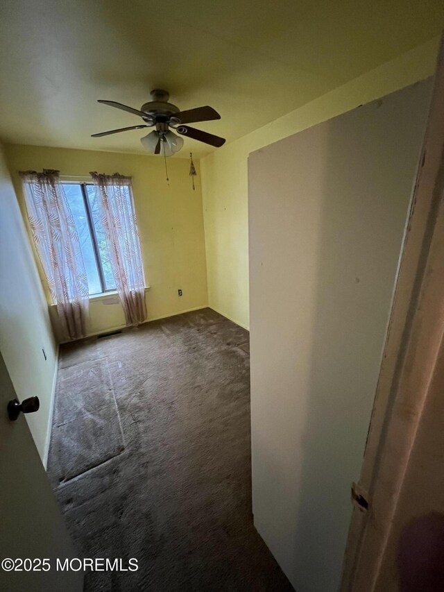 empty room with ceiling fan and dark carpet
